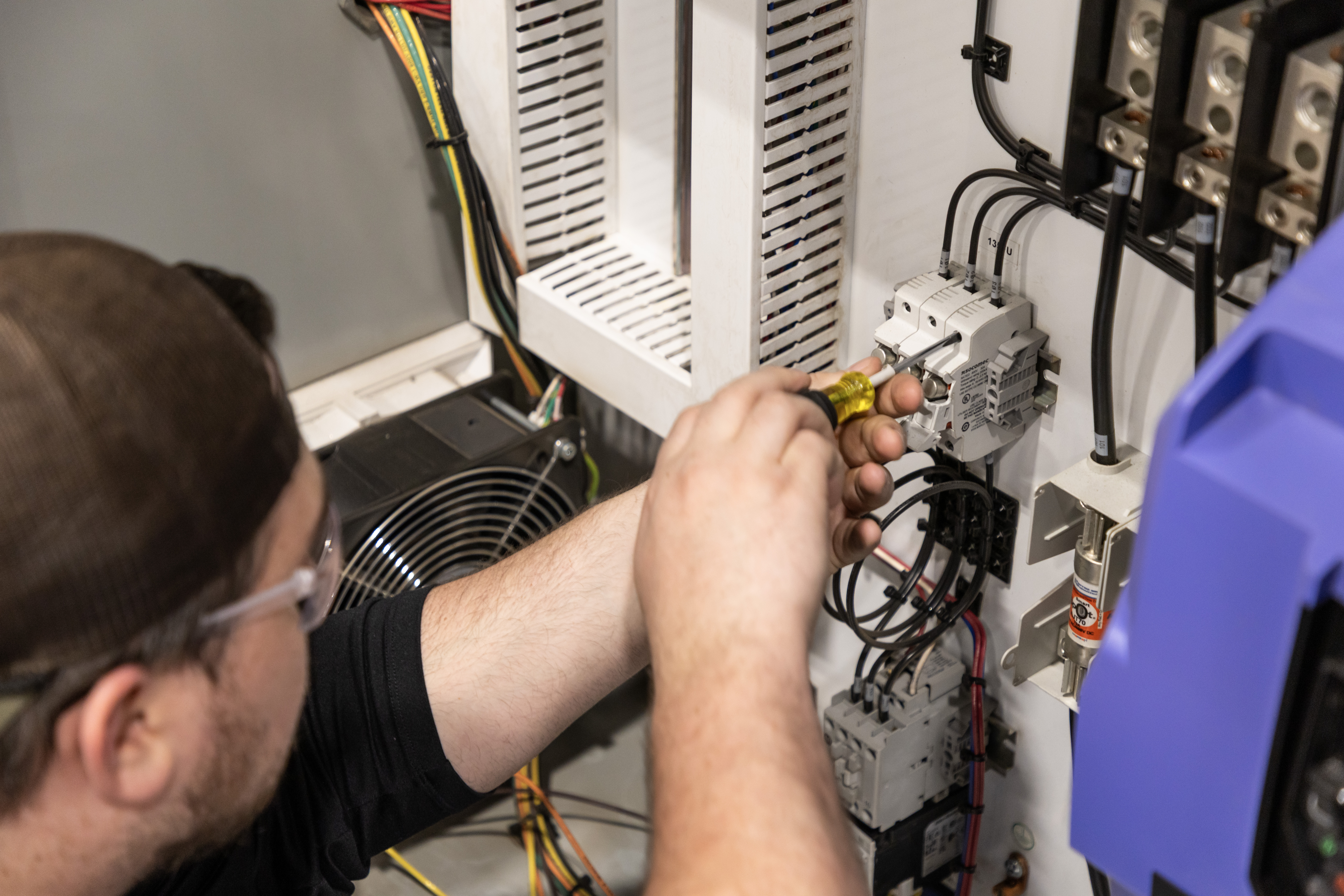 A person is using a screwdriver to screw a component into an electrical control panel.