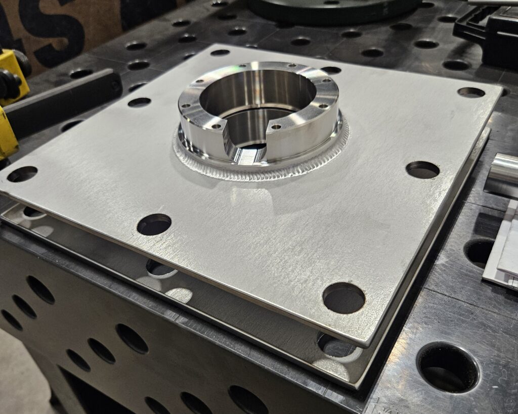 A circular metal component joined to a flat metal plate by a weld bead.