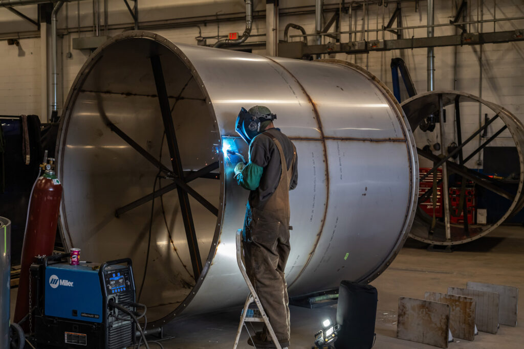 A person welds on a large piece if ductwork.