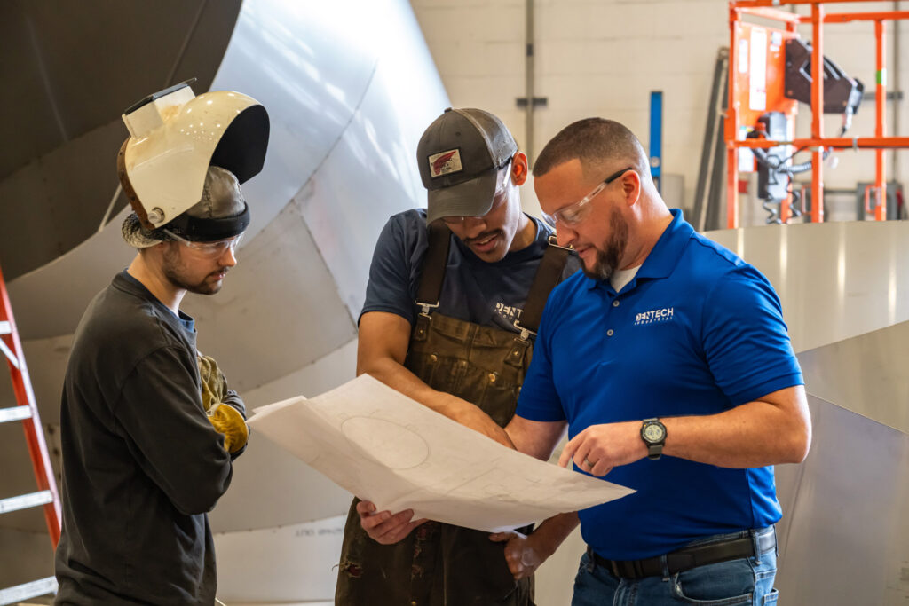 Three men look at a large piece of paper.