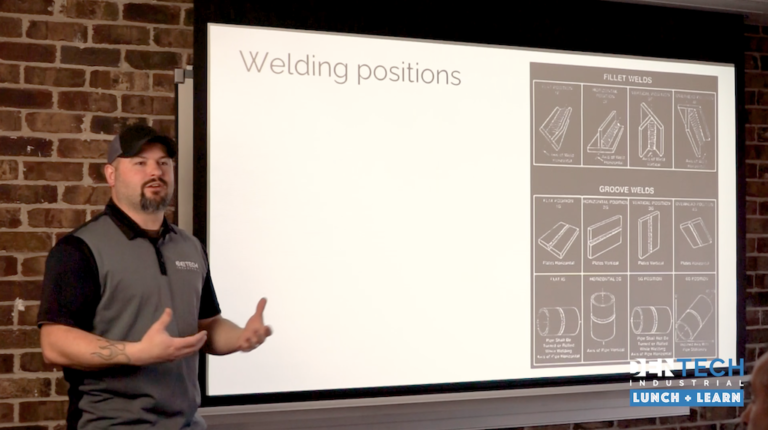 A man in a DenTech shirt stands at the front of the room to present about welding